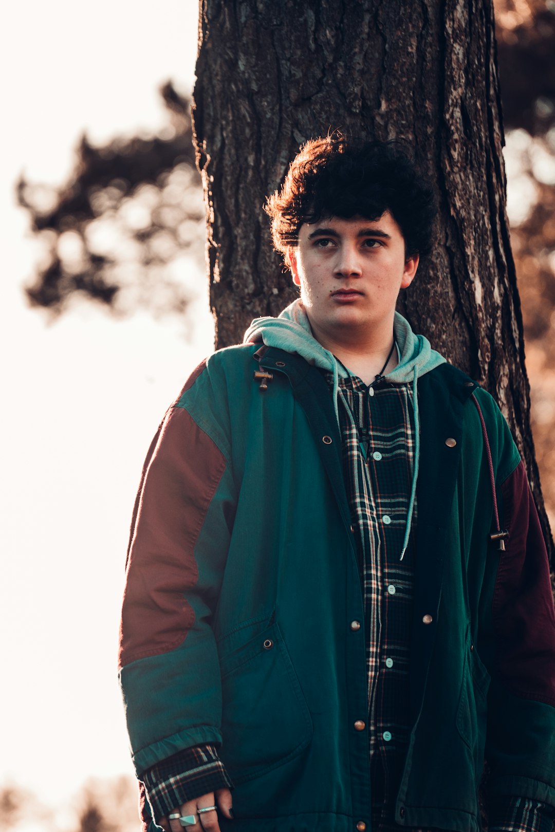 man in red zip up jacket standing beside brown tree during daytime