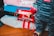 A close-up of a person wearing clothing with a bold red and white 'Supreme' logo. The attire includes a colorful, striped top and pants featuring the brand name in a repeated pattern. Several folded items, also displaying the logo, are stacked in the background.