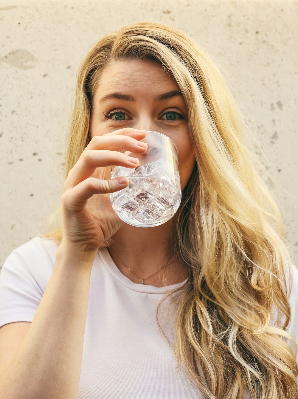 femme en chemise blanche à col rond boire de l’eau