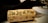 A close-up view of a wine cork lying on a table. The cork has 'The Joy of Wine' printed on it in bold letters. The background consists of a blurred black napkin and a part of a wine glass.