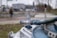 A close-up view of a metallic valve connected to several thick cables, with a blurred urban background. The focus is on the industrial component in the foreground, while figures and vehicles are indistinct in the distance.