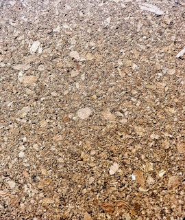 A close-up of a cork surface, showcasing a textured pattern composed of various shades of brown with visible granules and irregular shapes.