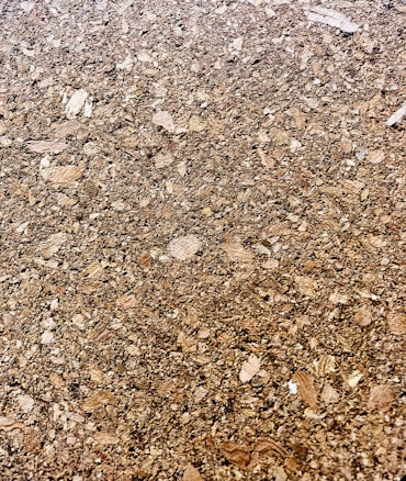 A close-up of a cork surface, showcasing a textured pattern composed of various shades of brown with visible granules and irregular shapes.