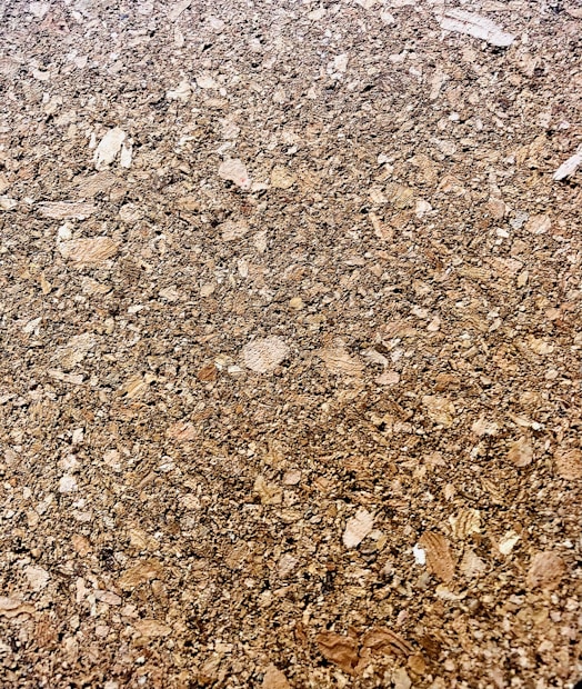 A close-up of a cork surface, showcasing a textured pattern composed of various shades of brown with visible granules and irregular shapes.