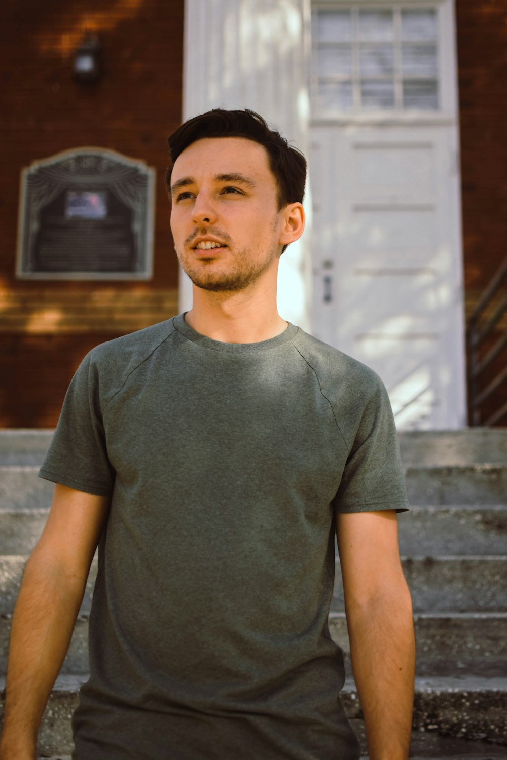 man in gray crew neck t-shirt standing near brown wooden wall during daytime