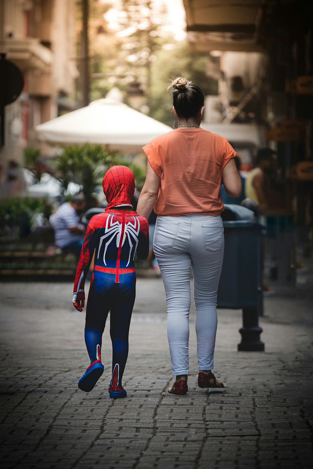 woman in red hoodie and blue denim jeans walking on sidewalk during daytime