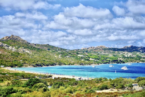 Green grass field near body of water under white clouds during daytime — Sardinia, Italy