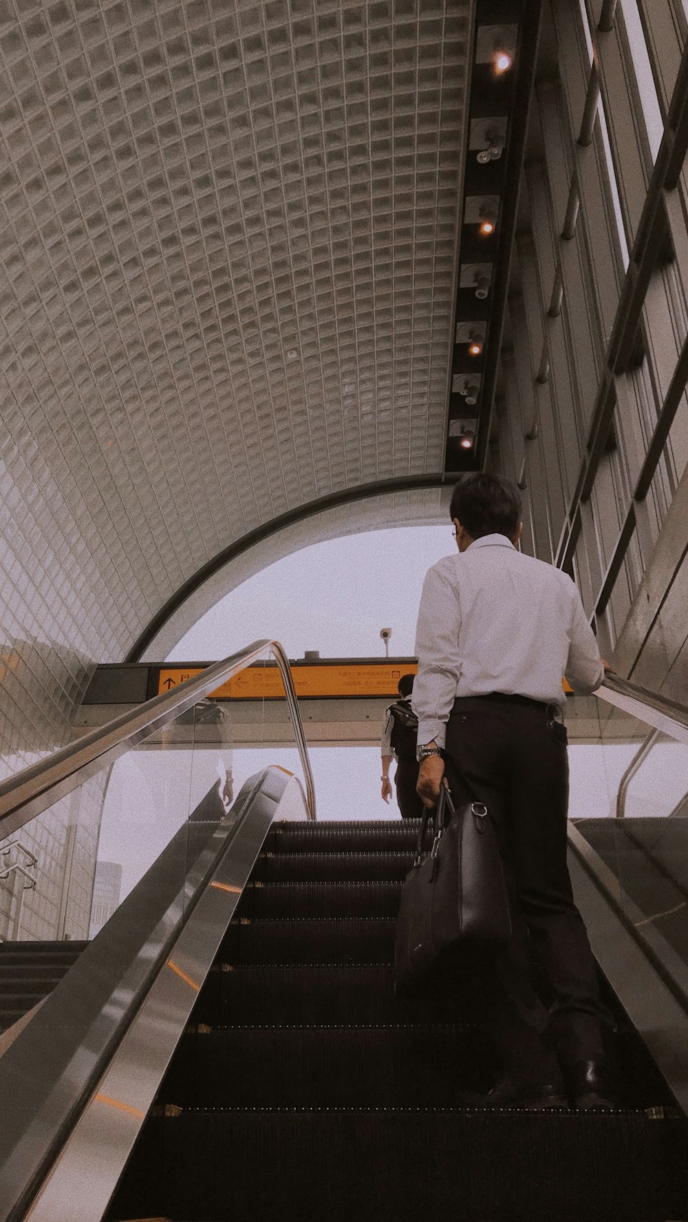 man in white dress shirt and black pants standing on black escalator