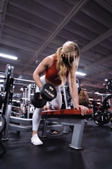 woman in black and red tank top and blue denim jeans sitting on bench press