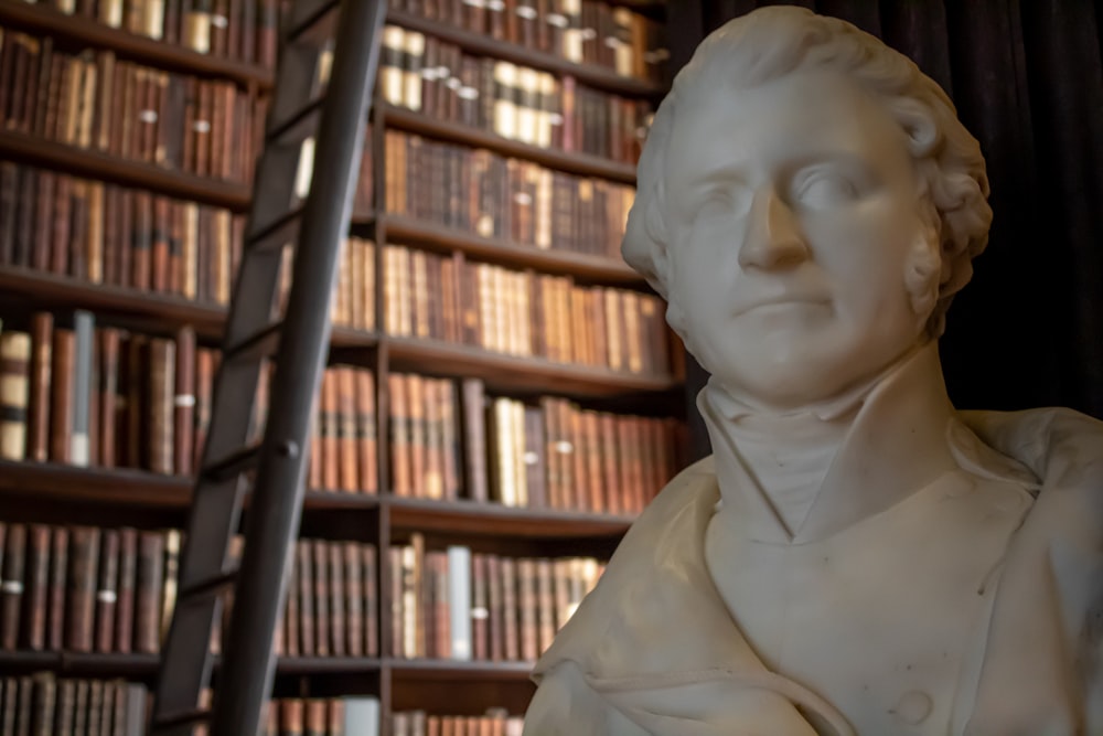 white bust of man near brown wooden book shelf