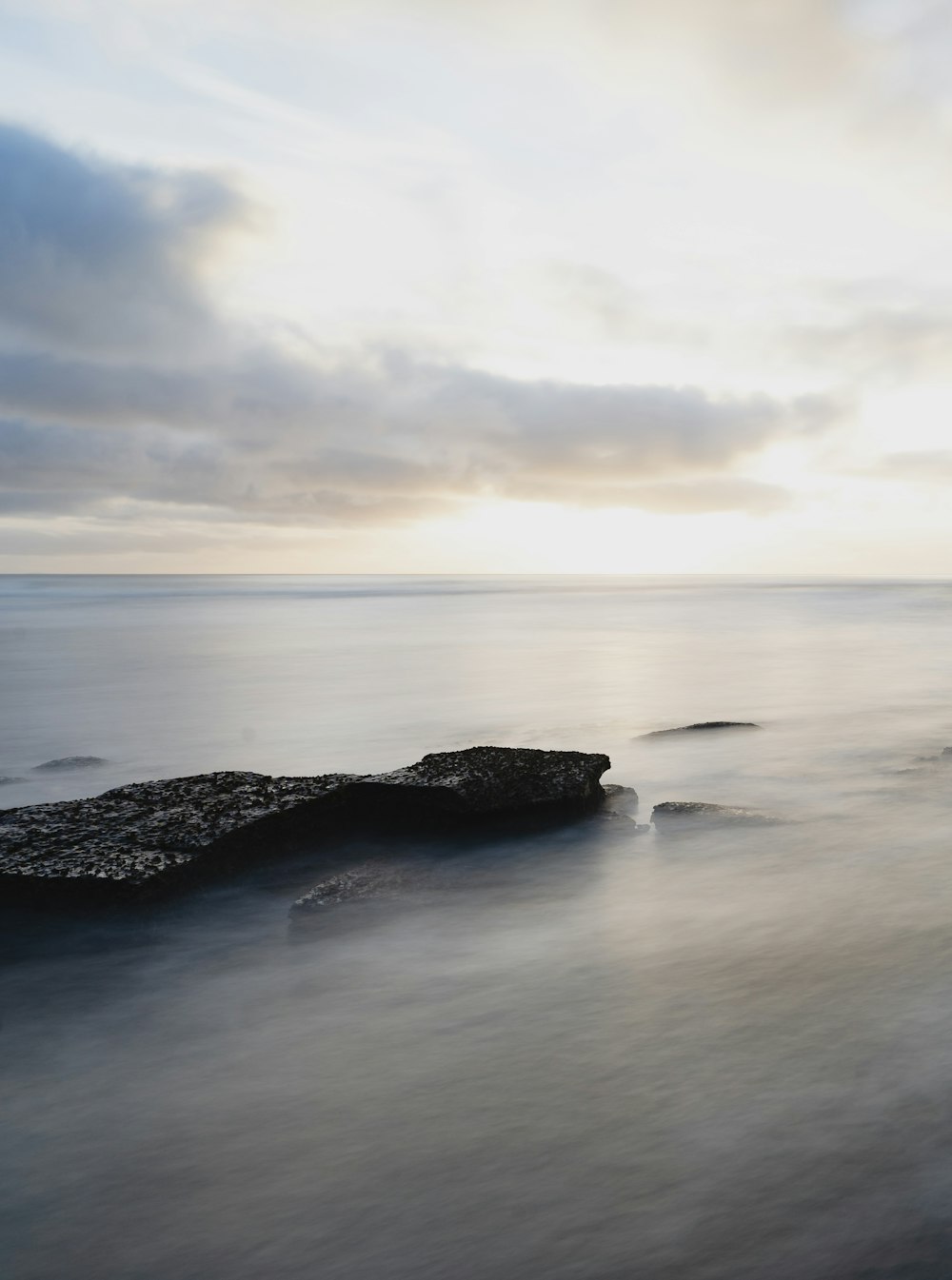 black rock formation on sea under white clouds during daytime