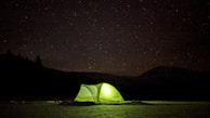 A small solar panel glowing under a starry night sky beside a tent.