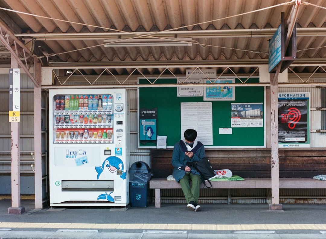 man in black jacket sitting on bench near vending machine