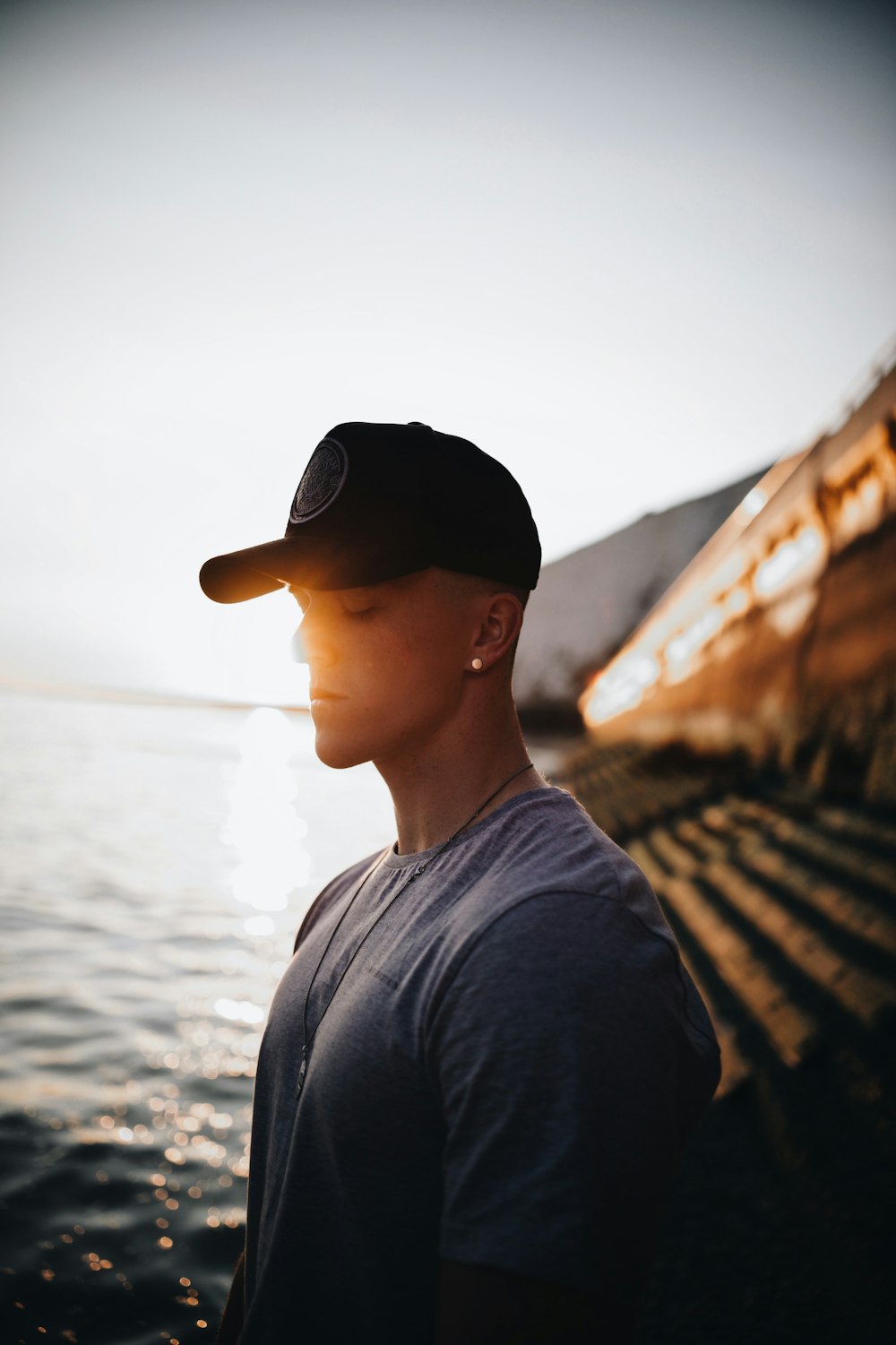 man in black crew neck shirt and black fitted cap standing on brown wooden bridge during