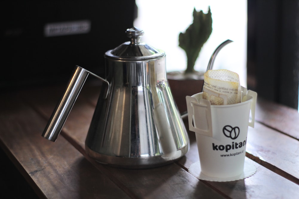 stainless steel teapot beside white ceramic mug on brown wooden table