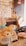 A cozy shop display featuring plush toys, with one prominently wearing a beige bow. Surrounding items include accessories and decorative pieces, with signs displaying prices. The warm lighting and lace tablecloth add a quaint and inviting atmosphere.