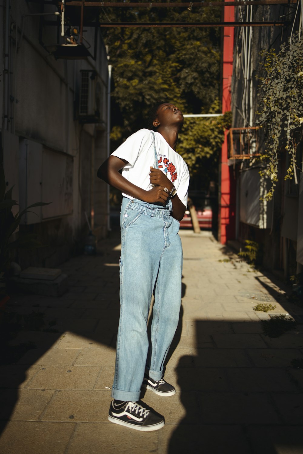 man in white t-shirt and blue denim jeans standing on sidewalk during daytime