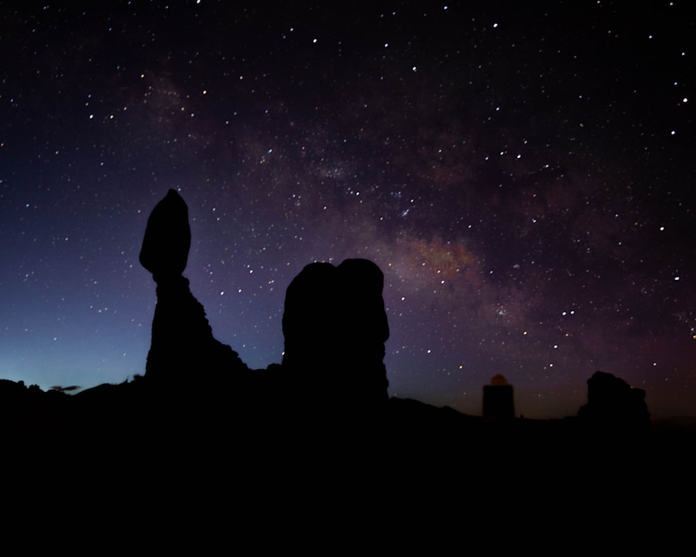 silhouette of person standing on rock formation under starry night