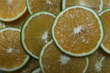 Slices of citrus fruits are arranged in a layered pattern. The slices display a gradient of yellow and green with thin white cores. The vibrant colors and fresh texture suggest a refreshing and juicy character.