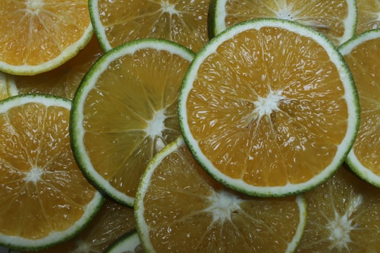 Slices of citrus fruits are arranged in a layered pattern. The slices display a gradient of yellow and green with thin white cores. The vibrant colors and fresh texture suggest a refreshing and juicy character.