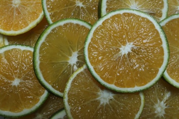 Slices of citrus fruits are arranged in a layered pattern. The slices display a gradient of yellow and green with thin white cores. The vibrant colors and fresh texture suggest a refreshing and juicy character.