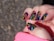 A close-up of a hand with nails painted in a vibrant, glittery spiral pattern. The design features colors like yellow, purple, blue, red, and green against a black background. The spiral patterns are bold and eye-catching, with each nail showcasing a similar but slightly varied design. A pink sleeve partially covers the wrist, suggesting the person is wearing a pink garment.