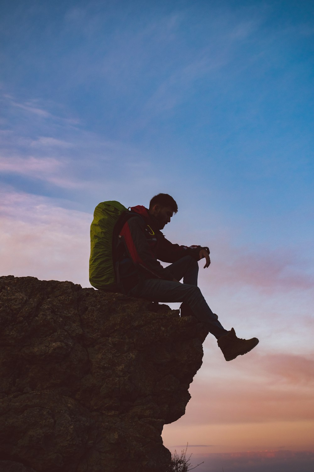 man in green jacket sitting on rock during daytime