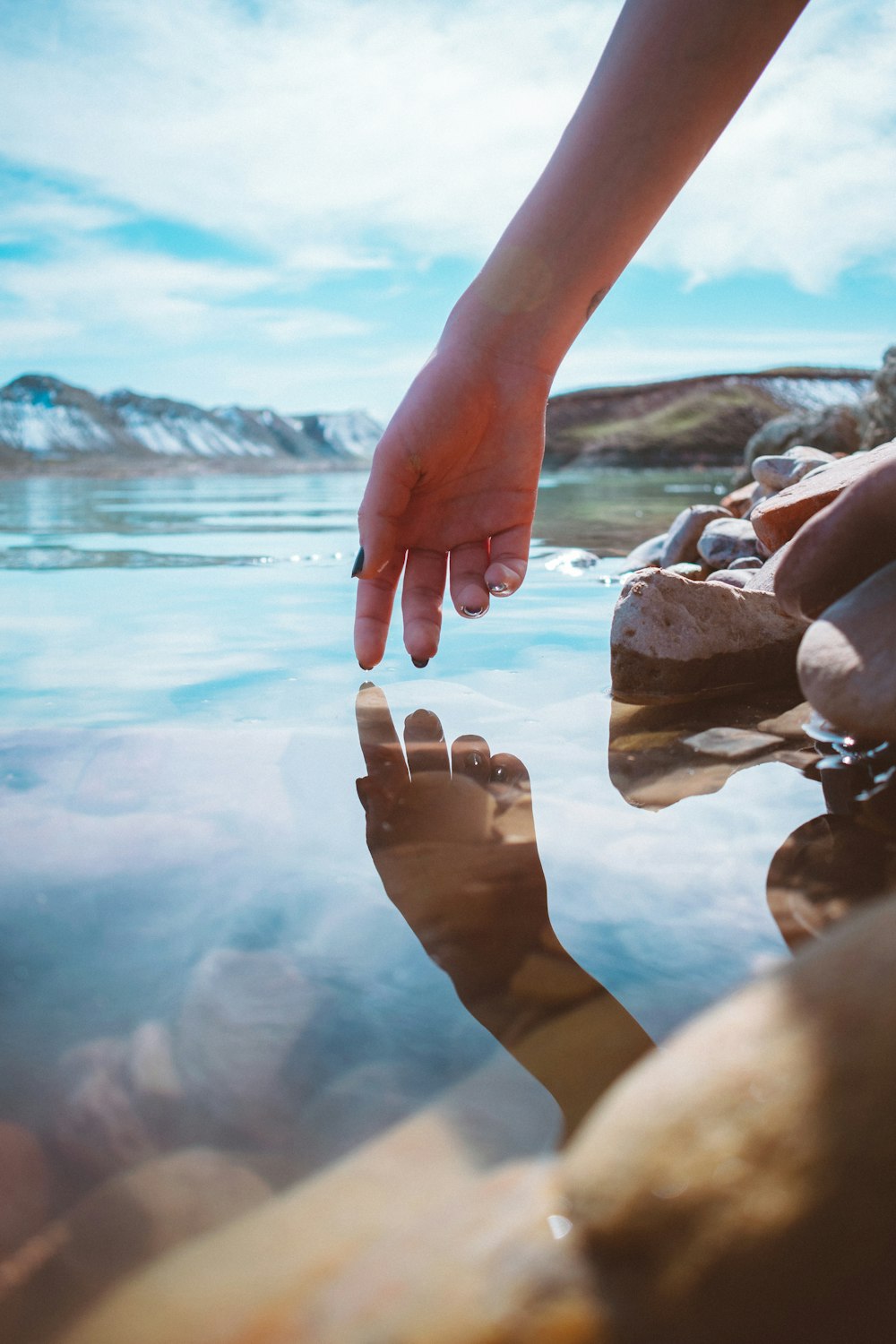 personne avec du vernis à ongles brun tenant des pierres près d’un plan d’eau pendant la journée