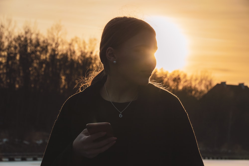 mulher na camisa preta segurando o smartphone durante o pôr do sol