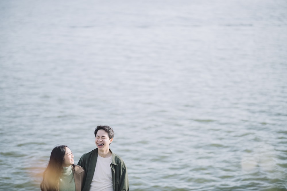 uomo e donna che sorridono accanto allo specchio d'acqua durante il giorno