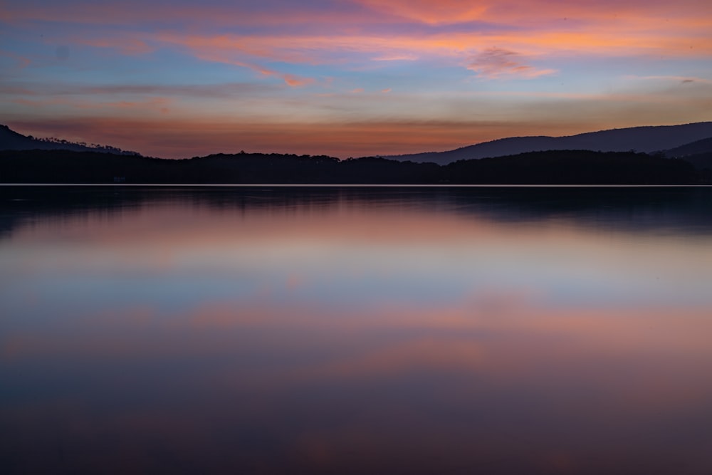 body of water near mountain during sunset