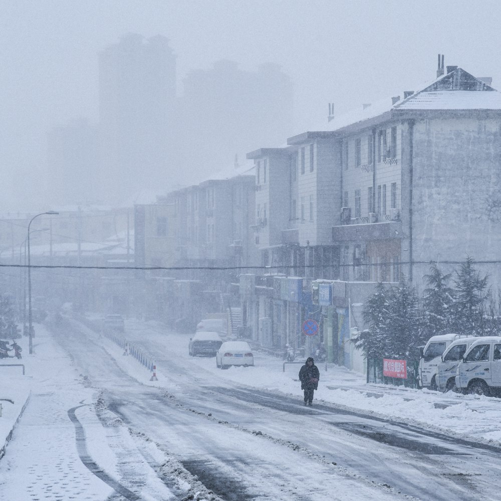 person walking on snow covered road near cars and buildings during daytime