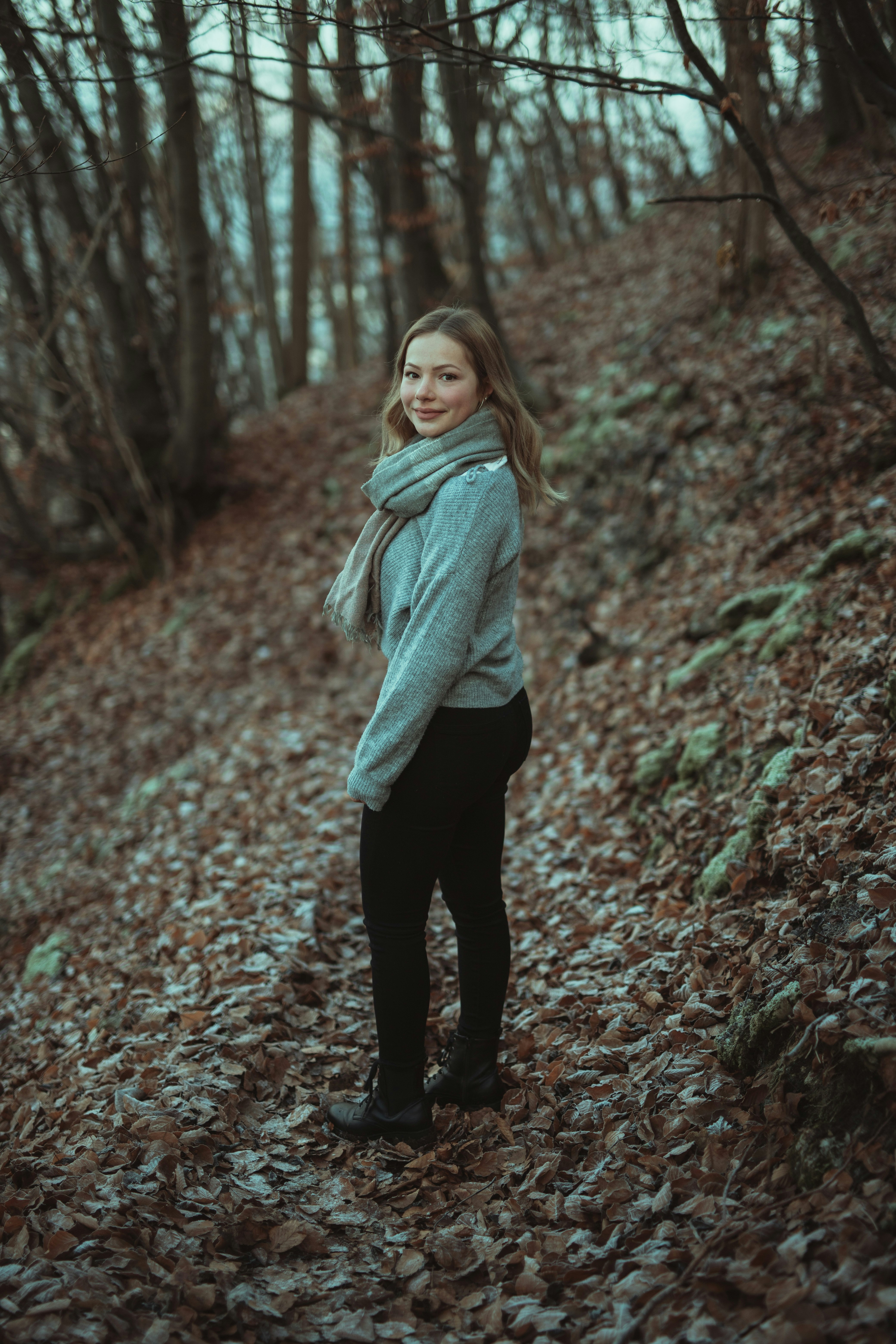 woman in gray sweater and black pants standing on forest during daytime