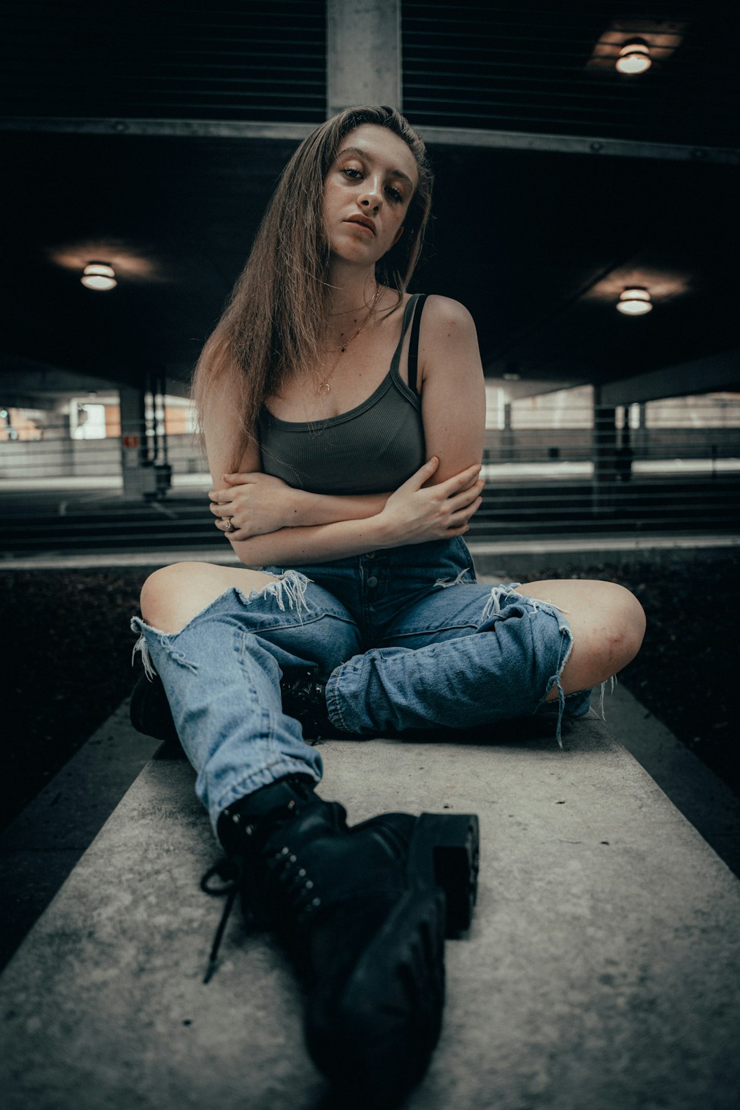 woman in black tank top and blue denim jeans sitting on sidewalk during night time