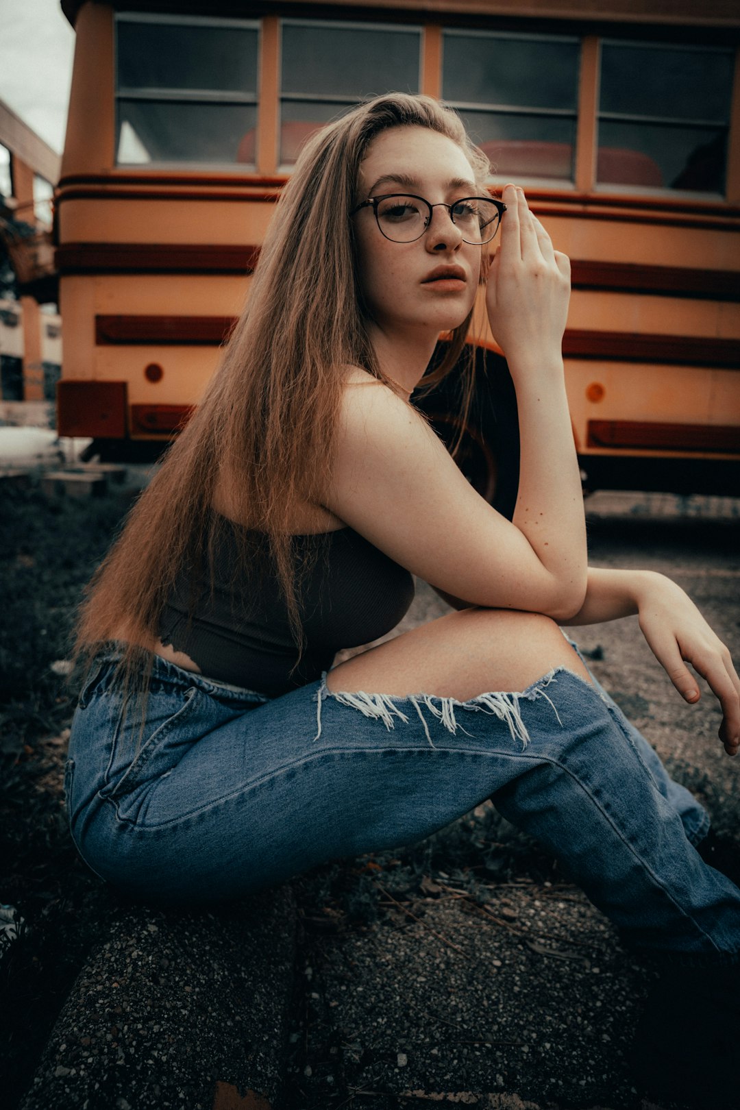 woman in black tank top and blue denim jeans sitting on brown wooden bench during daytime