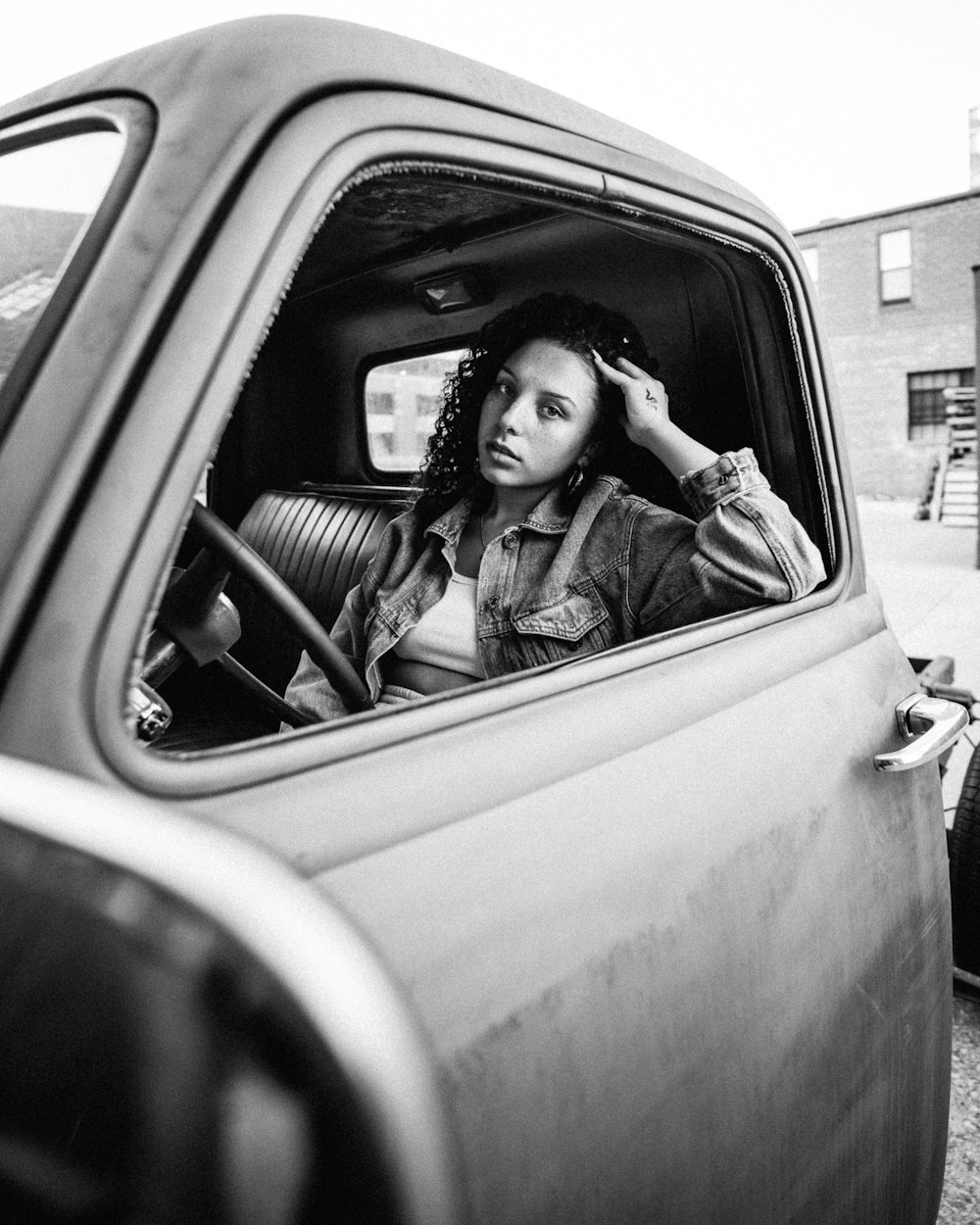 grayscale photo of woman in jacket sitting on car