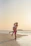 A couple dancing passionately on the beach at sunset with gentle ocean waves behind them.