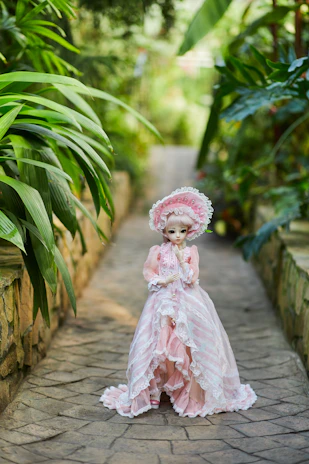 Close-up of a petite doll dressed in hand-stitched clothing, standing beside a miniature garden.