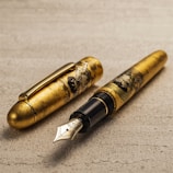 A luxurious fountain pen with intricate gold detailing featuring artistic engravings on the body. The pen is placed on a textured surface, and the cap is detached, displaying the polished nib.