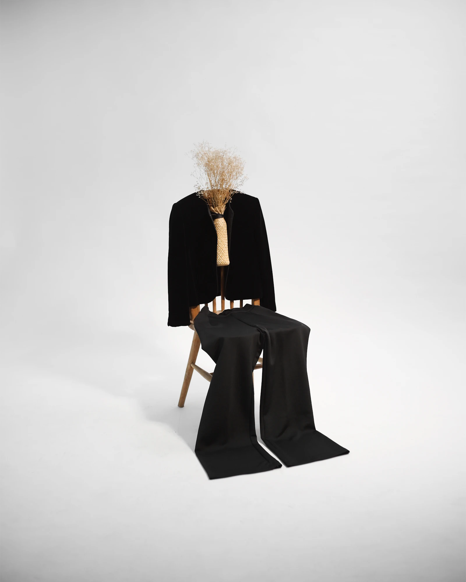 Woman in a minimalist black coat sitting on a wooden chair