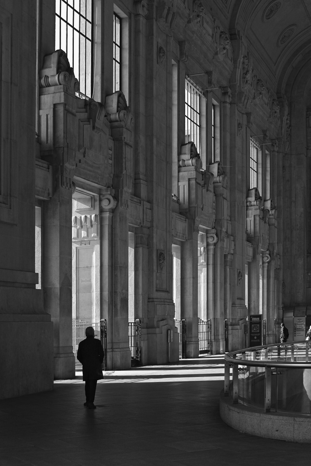 grayscale photo of man in black jacket walking on sidewalk