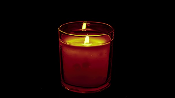 Glass candle holder with a flickering candle casting gentle light on a wooden table.
