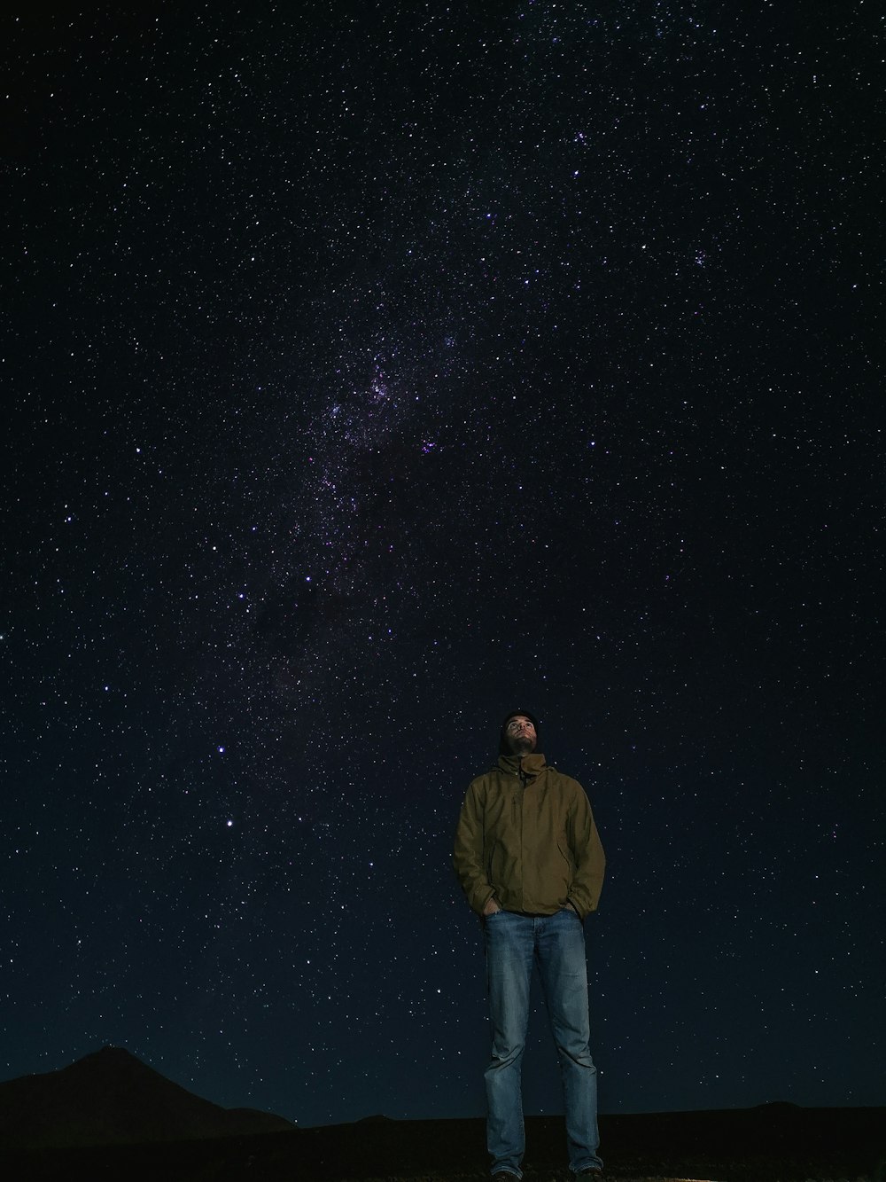 Hombre con chaqueta marrón de pie bajo la noche estrellada