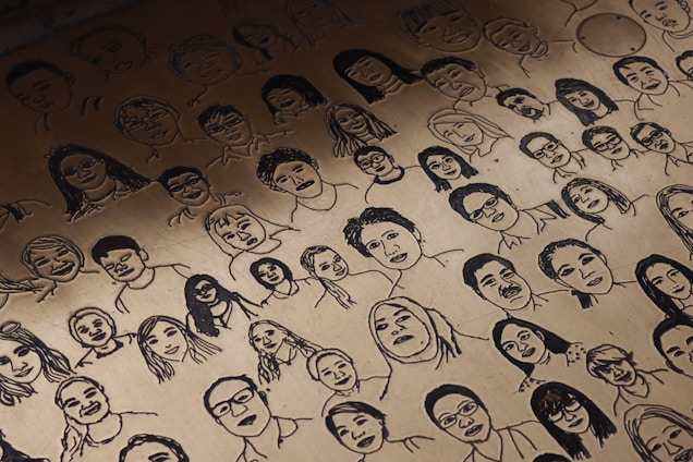 A detailed collection of sketched faces covering a surface. Each face is uniquely drawn with varying expressions and hairstyles, resembling a large portrait montage.