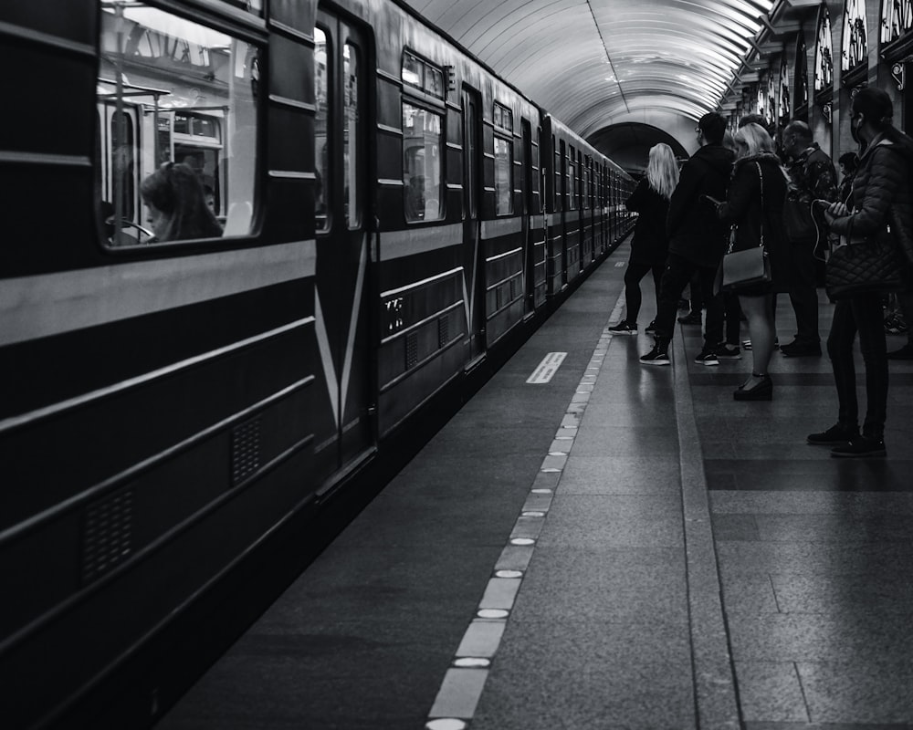 Foto in scala di grigi di persone che camminano sulla stazione ferroviaria