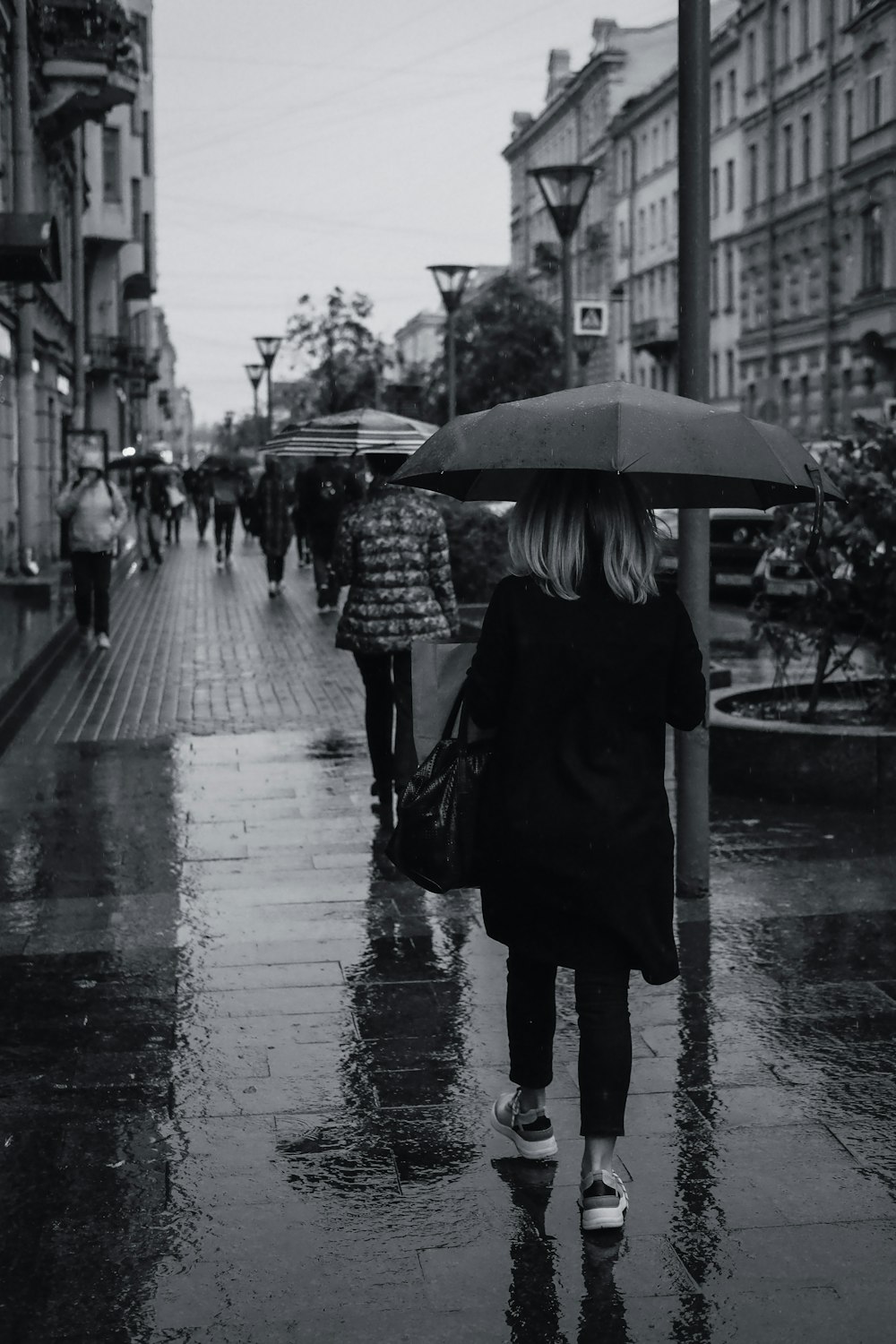 woman in black coat holding umbrella walking on sidewalk during daytime