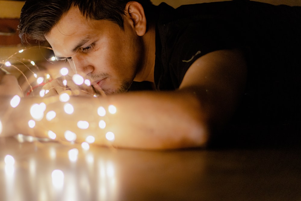 man in black crew neck shirt holding lighted string lights