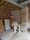 A partially constructed room with exposed brick and wooden beams. Building materials like boards and cardboard boxes are stacked against the walls. Scaffolding supports are placed in the middle, draped with a cloth. The floor is concrete, and tools or equipment can be seen around.
