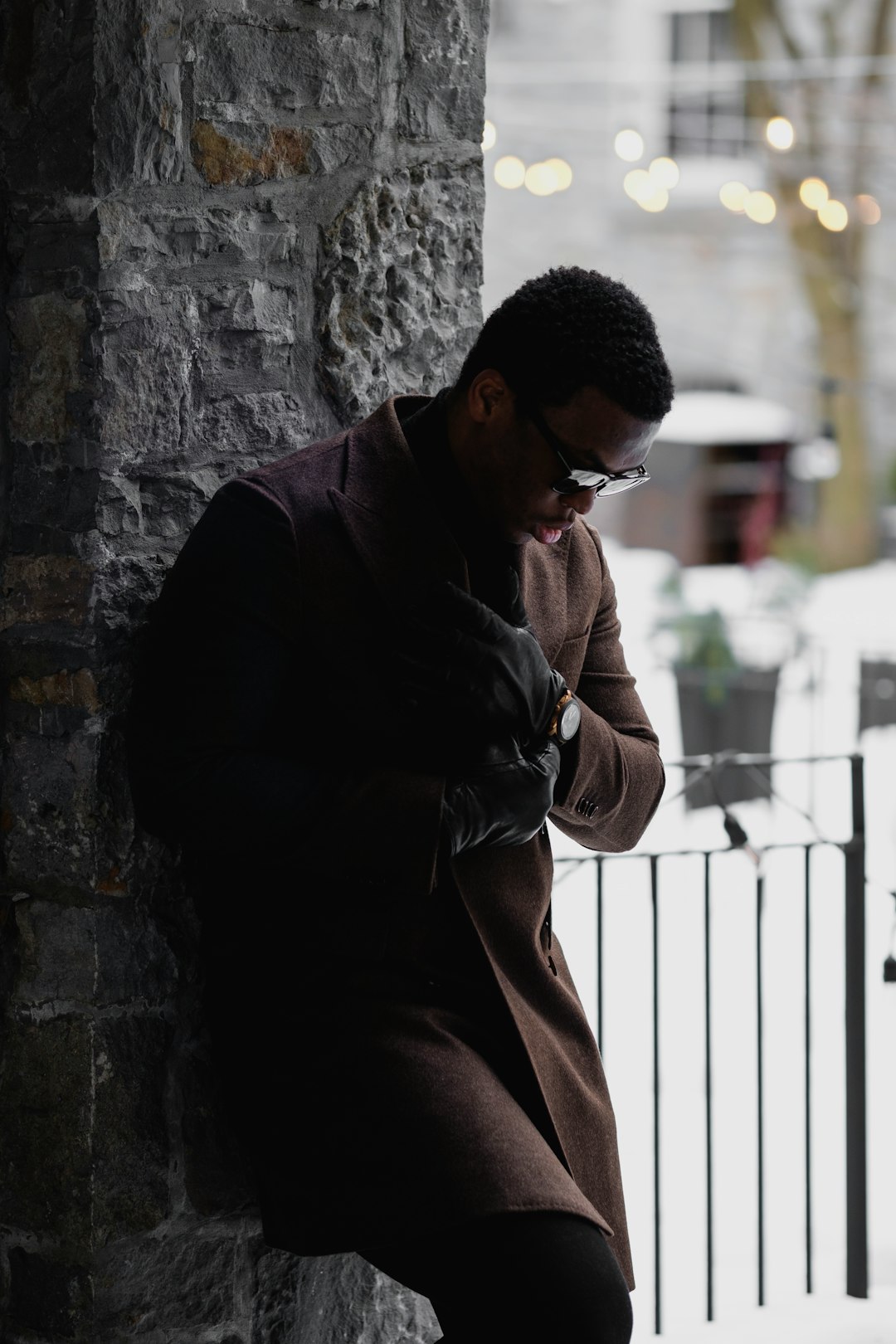 man in black jacket and brown pants sitting on concrete wall during daytime