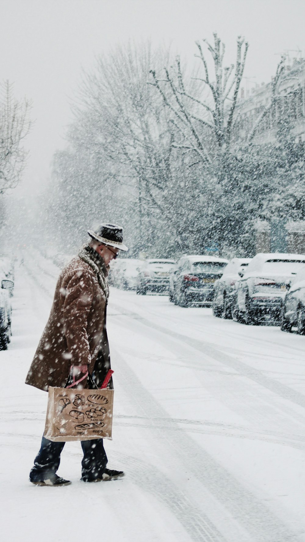 昼間、雪に覆われた地面に立つ茶色のコートを着た人